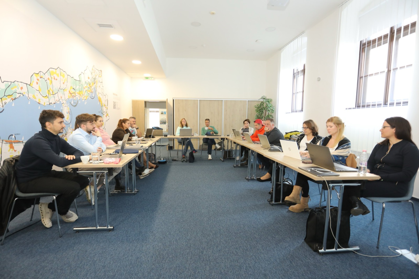 01: AI training in the VisitBalaton365 training room in Keszthely; participants working on laptops, the AI slide on the screen, the map of Lake Balaton on the wall. 02: VisitBalaton365 DMO staff at the U-shaped tables during the AI training, in front of the Lake Balaton map wall. 03: Participants practicing AI tools on laptops during the training. 04: The full group of the training room at work. 05: DMO staff attentively following the AI training demo.