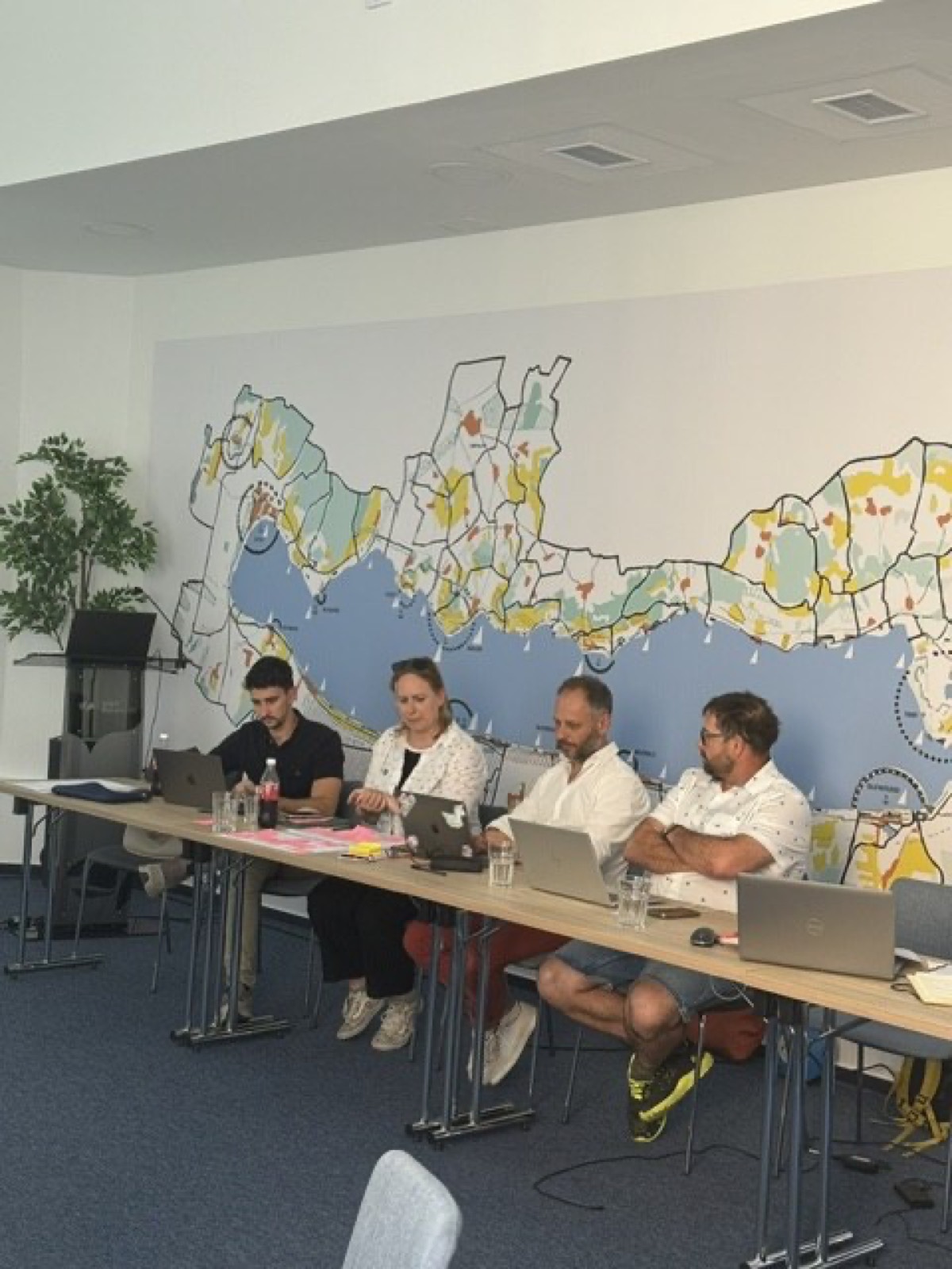01: Adam Schmutz giving a talk on package pricing at VisitBalaton365's Keszthely training center; in the foreground the “Package creation” canvas with participants' notes. 02: The Keszthely training room with the Lake Balaton map on the wall; participants at the two-day workshop, the title slide on the screen. 03: Small-group work next to the VisitBalaton365 banner and the projected canvas template. 04: Participants following a package example on the projector. 05: The Keszthely training room from above, participants at the U-shaped tables in front of the Lake Balaton map wall. 06: A small group working together on the package canvas. 07: Participants working over the package-planning template at the long table. 08: A lively discussion in a four-person group. 09: Workshop participants in a small-group consultation with notes and a canvas. 10: Participants at the training room table in front of the Lake Balaton map.