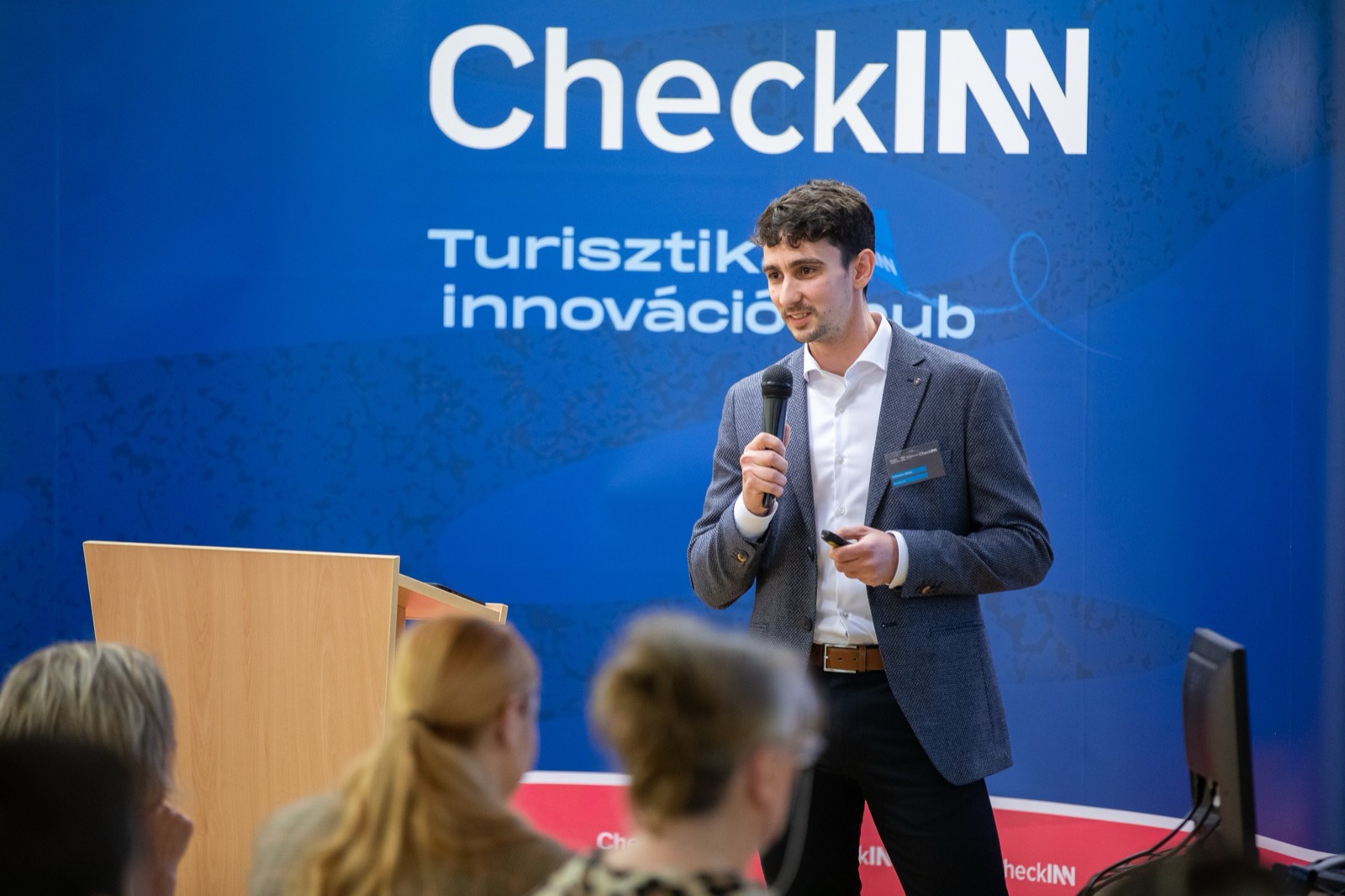 01: Adam Schmutz speaking with a microphone in front of the CheckINN banner, with the audience in the foreground. 02: Adam Schmutz mid-talk, the CheckINN Tourism Innovation Hub banner in the background. 03: Adam Schmutz presenting to the workshop audience in front of the CheckINN backdrop. 04: The full lecture hall with the audience; Adam Schmutz on stage by the CheckINN banner. 05: Round-table discussion: Adam Schmutz and the moderator in front of the METU backdrop. 06: The participants of the workshop's round-table discussion in front of the Budapest Metropolitan University banner. 07: Adam Schmutz during a professional conversation in a break of the event.